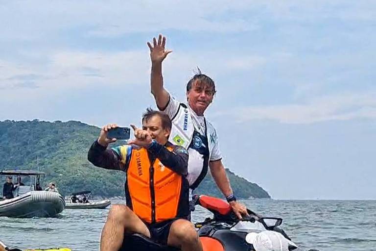 Acompanhado pelo assessor especial Tenente Mozart Aragão, o presidente Jair Bolsonaro acena para apoiadores no litoral paulista