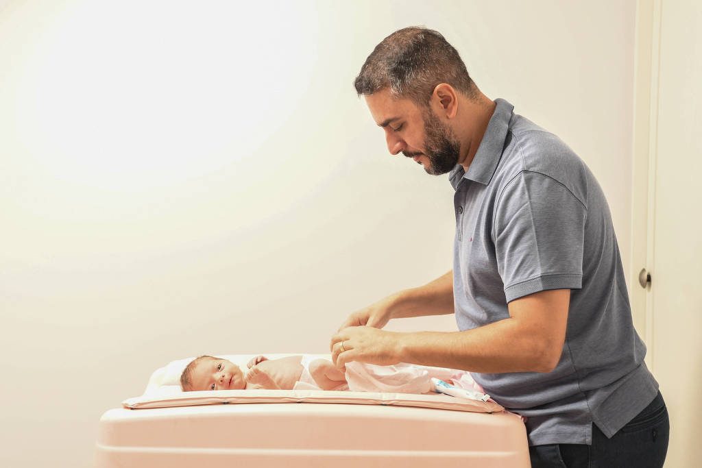 Felipe Martines Rocha, 36, químico, troca as fraldas da filha Cecília, de 20 dias