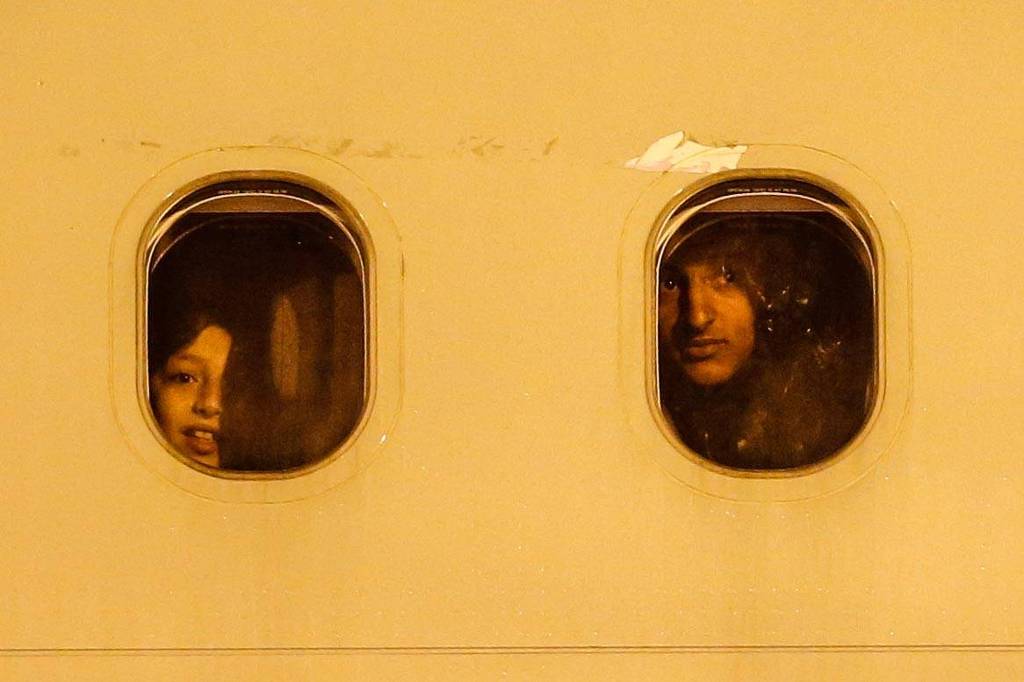 Criança e mulher que estavam na Faixa de Gaza olham pela janela de avião da FAB ao pousarem em Brasília